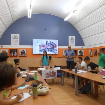 Personas en una sala de conferencias prestando atención a una presentación con pantalla en un entorno educativo.