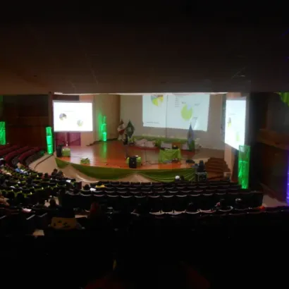 Auditorio con presentación de diapositivas proyectadas y asistentes sentados.