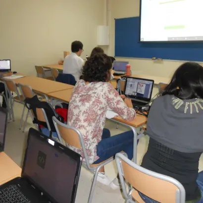 Estudiantes en aula usando laptops, atentos a una presentación en proyector.