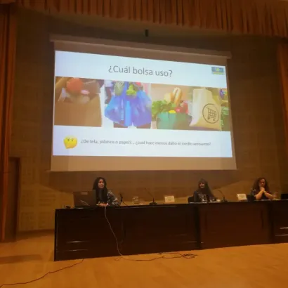 Presentación sobre el uso de bolsas ecológicas en un auditorio con tres personas en la mesa principal.