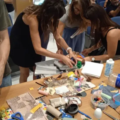 Personas hacen manualidades en una mesa llena de materiales como papel, tijeras y cinta adhesiva.