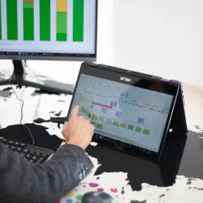 Persona usando una computadora portátil y señalando una gráfica en la pantalla táctil, con otra pantalla al fondo.