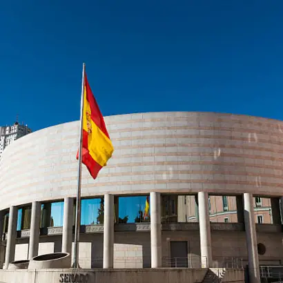 Fachada del Senado de España con una bandera española ondeando al frente, bajo un cielo despejado.