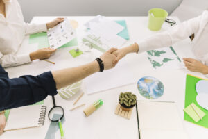 Personas dándose la mano sobre un escritorio con papeles y mapas verdes relacionados con sostenibilidad.